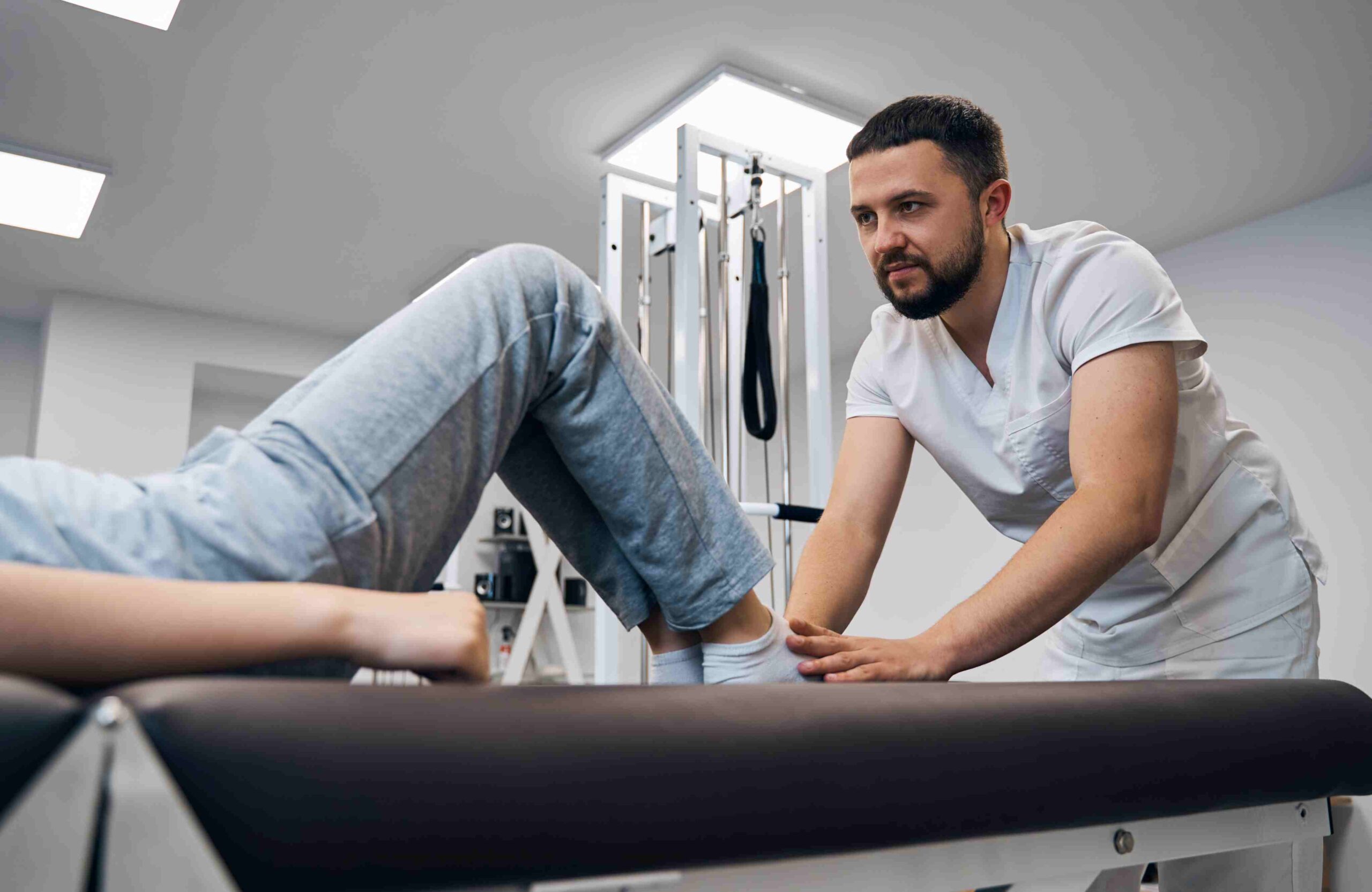 Physiotherapeut behandelt das Knie eines Patienten auf einer Behandlungsliege